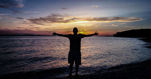 Silhouette woman standing by sea against sky during sunset