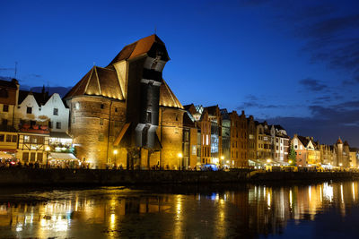 Illuminated buildings by river against sky at night