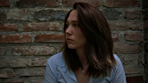 Close-up of thoughtful young woman looking away while standing against brick wall