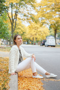 Full length of woman sitting on tree during autumn