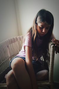 Girl sitting on chair against wall