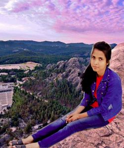 Portrait of woman sitting on rock against mountains