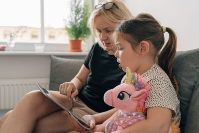 Woman teaching girl through digital tablet at home