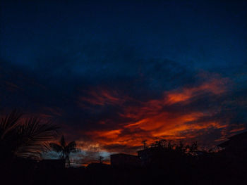 Low angle view of silhouette trees and buildings against dramatic sky