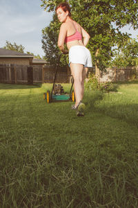 Full length of woman with lawn mover in yard