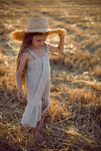Girl child with long hair walking across the field wearing a hat with long hair during sunset