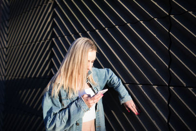 Woman using mobile phone by wall