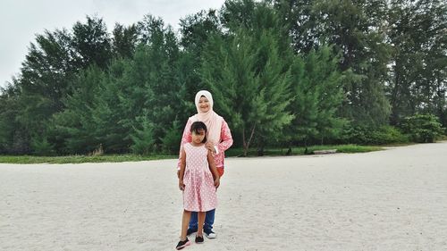 Portrait of happy mother with daughter standing against trees