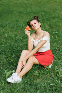 A young happy woman in a red skirt and a white t-shirt blows a kiss while holding a watermelon 