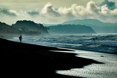 Silhouette person standing on sea shore against sky