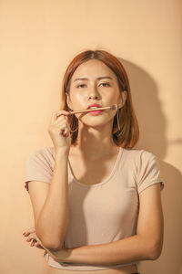 Portrait of young woman with make-up brush standing against wall