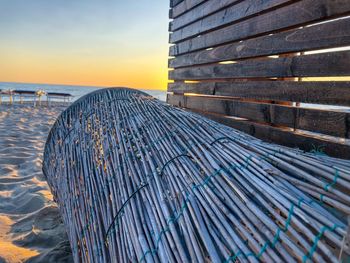 Metallic structure on beach against sky at sunset