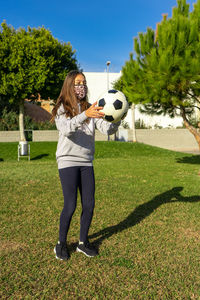 Full length of girl wearing mask playing with soccer ball in park