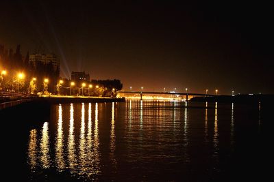 Illuminated city by river against sky at night