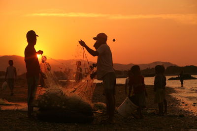 Fishermen standing by fishing net against sky during sunset