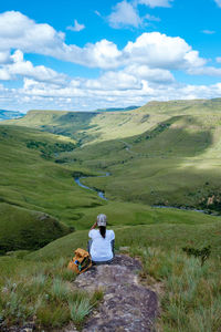 Rear view of man sitting on mountain against sky