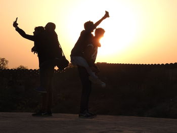 Silhouette friends taking selfie against clear sky during sunset