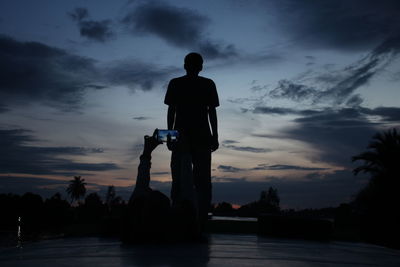 Silhouette man photographing against sky during sunset