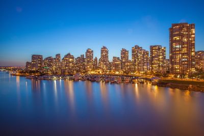 Illuminated cityscape by sea against clear sky at night