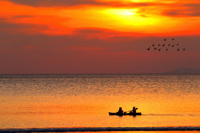 Silhouette birds on sea against orange sky