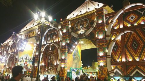 Low angle view of illuminated ferris wheel against buildings at night