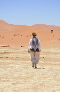 Rear view of woman walking on desert during sunny day