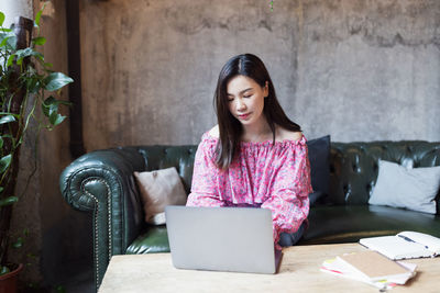 Young woman using mobile phone while sitting on wall