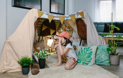 Girl playing with cardboard binoculars while camping at home