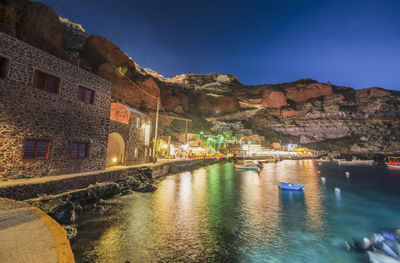 Illuminated buildings by canal against sky at night