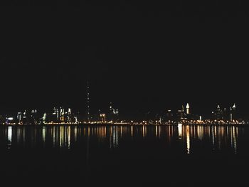 Illuminated buildings by river against sky at night