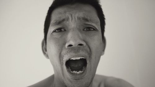 Close-up portrait of frustrated man shouting against wall