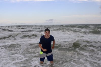 Full length of teenage boy standing at beach against sky