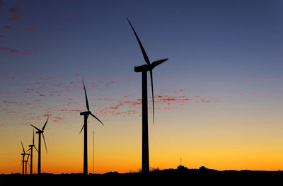 Silhouette windmills on field against sky during sunset