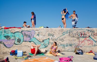 Full length of friends sitting against clear blue sky