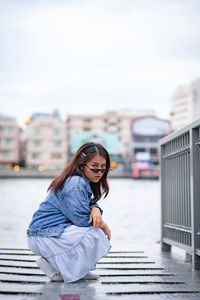 Portrait of young woman on railing against sky