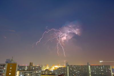 Lightning over illuminated buildings in city at night