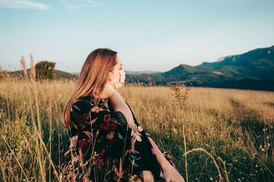 Young woman standing on field against sky