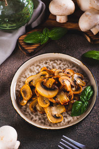 Savory appetizer of fried champignon mushrooms with basil on a plate on the table vertical view