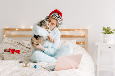 Woman in santa hat kissing cute puppy dog pet. woman calling family friends on video call online 