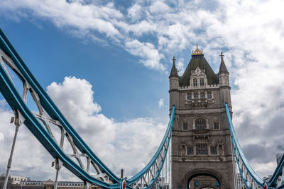 Low angle view of bridge and buildings against cloudy sky