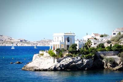 Buildings by sea against clear blue sky