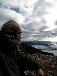 Side view of man sitting against cloudy sky