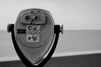 Close-up of coin-operated binoculars by sea against sky