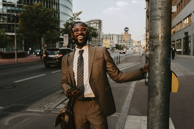 Smiling male entrepreneur standing by pole on footpath in city