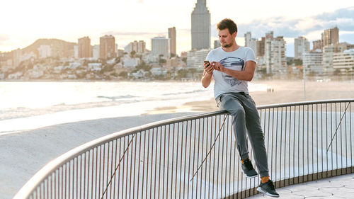 Full length of young man holding railing against buildings in city