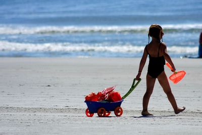 Rear view of girl pulling cart at beach