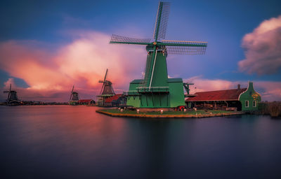 Traditional windmills by lake against cloudy sky
