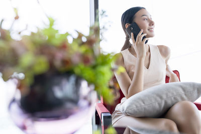 Young woman using mobile phone while sitting on wall