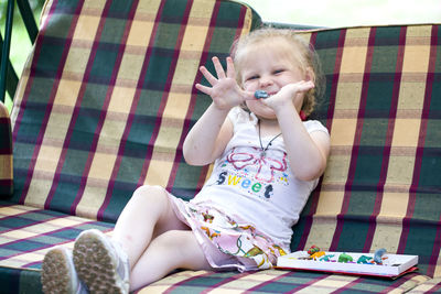 Full length portrait of playful girl sitting on sofa at home