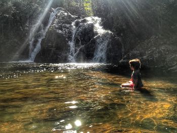 Full length of woman splashing water in waterfall